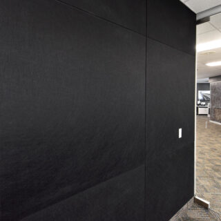 A black Ezobord Full Sheet acoustic wall panel installed in a modern office setting, providing sound absorption and privacy.